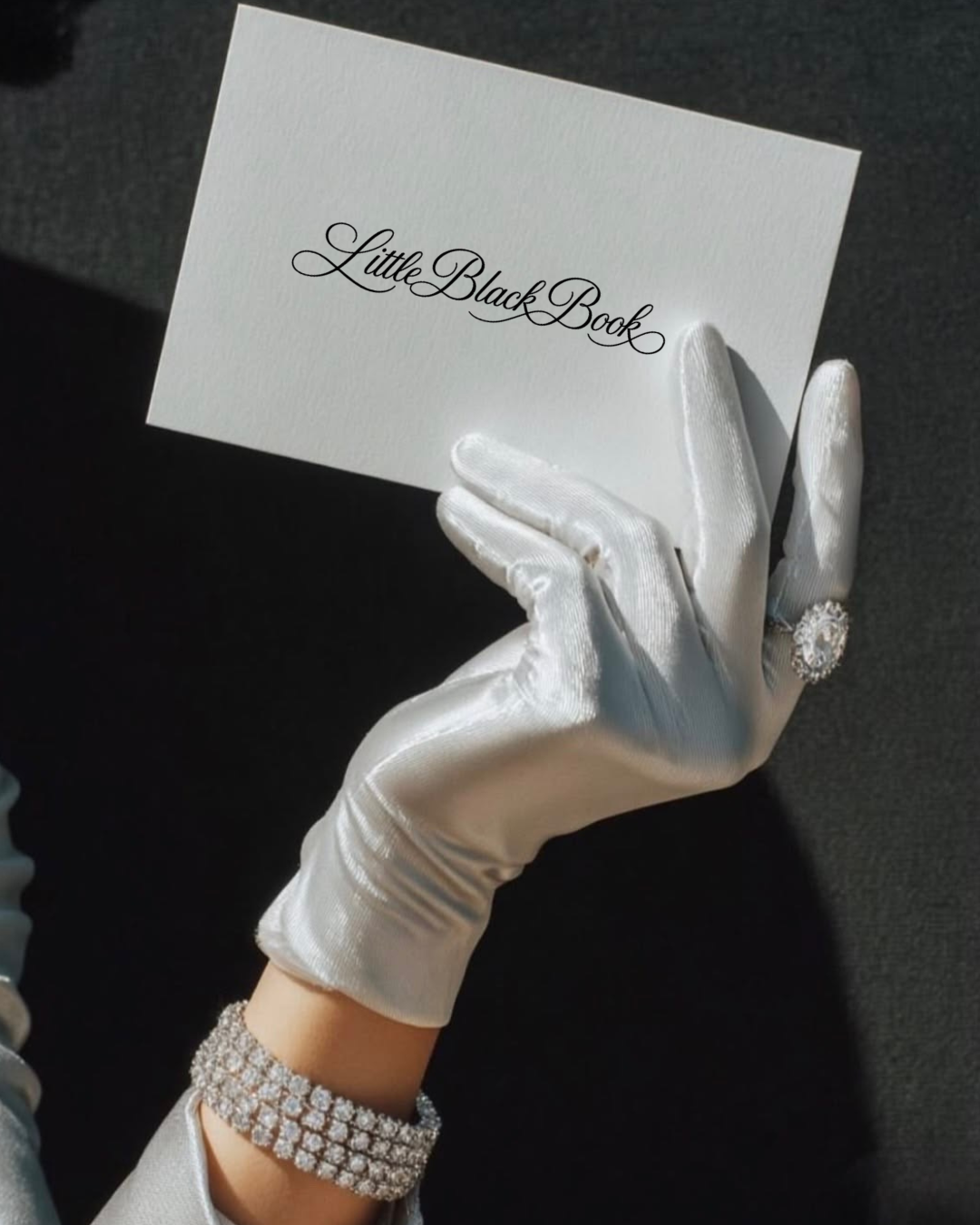 A gloved hand holding a card reading Little Black Book